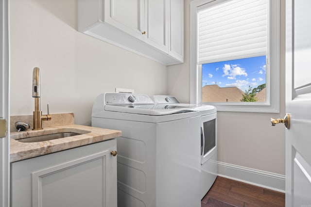 clothes washing area featuring washing machine and dryer, baseboards, dark wood finished floors, a sink, and cabinet space