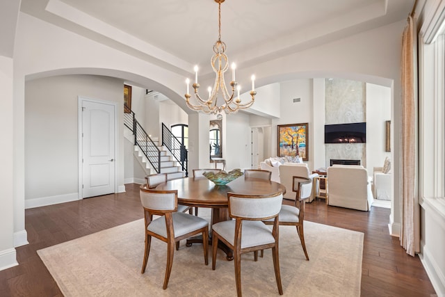dining room with arched walkways, dark wood-style flooring, a notable chandelier, and stairway
