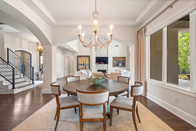 dining room featuring a tray ceiling, wood-type flooring, arched walkways, and baseboards
