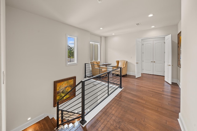 corridor with wood-type flooring, baseboards, an upstairs landing, and recessed lighting