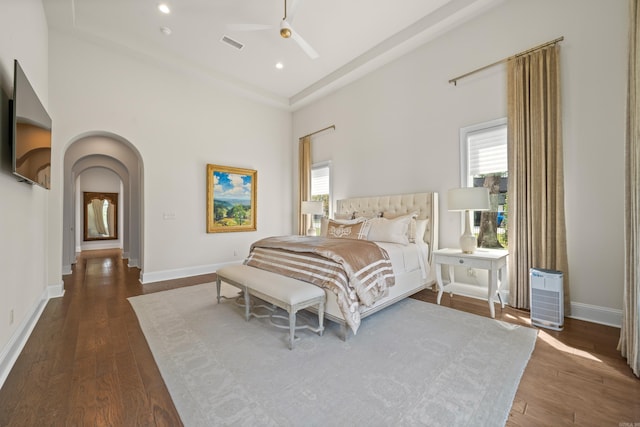 bedroom with baseboards, visible vents, a towering ceiling, dark wood-type flooring, and arched walkways