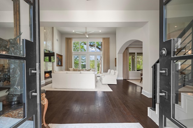 foyer with a ceiling fan, baseboards, hardwood / wood-style flooring, arched walkways, and a large fireplace