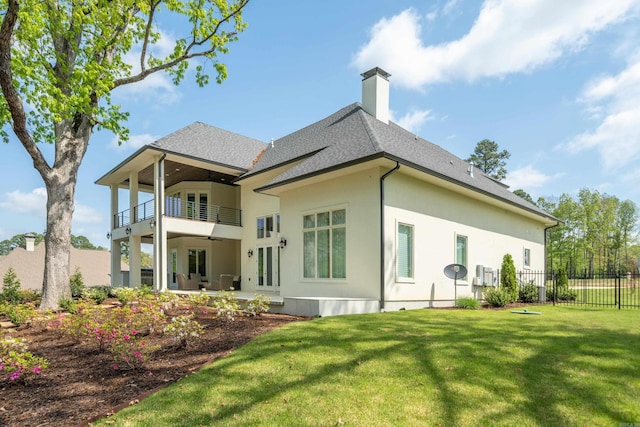 rear view of house featuring a balcony, a chimney, fence, and a lawn