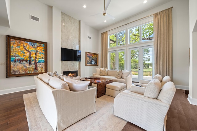 living area featuring ceiling fan, visible vents, baseboards, and a high ceiling