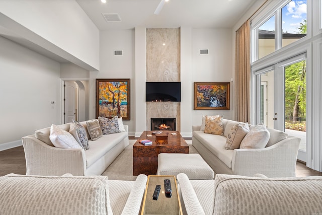 living area with a premium fireplace, baseboards, visible vents, wood finished floors, and a high ceiling