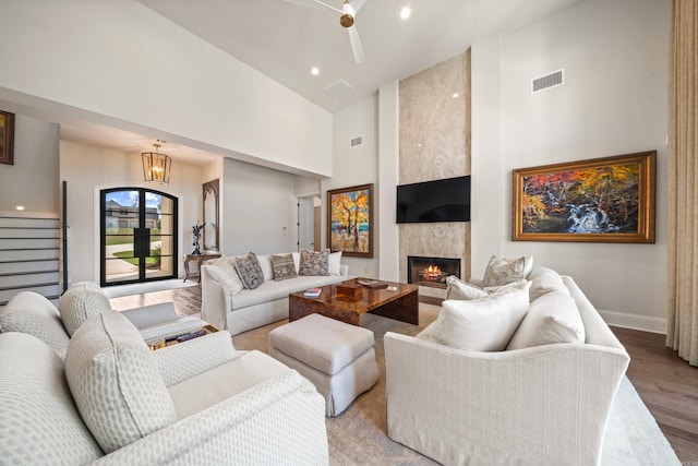 living room featuring wood finished floors, high vaulted ceiling, a premium fireplace, visible vents, and baseboards