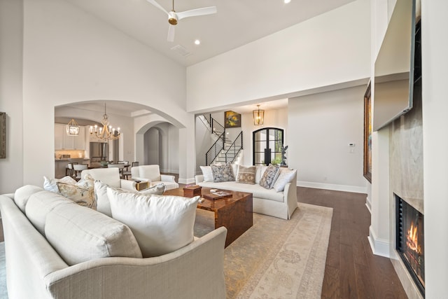 living area featuring high vaulted ceiling, a lit fireplace, arched walkways, stairway, and dark wood-style floors
