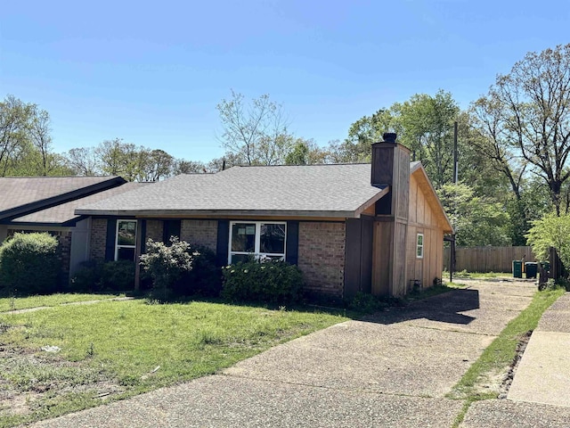 ranch-style house with roof with shingles, fence, brick siding, a front lawn, and a chimney