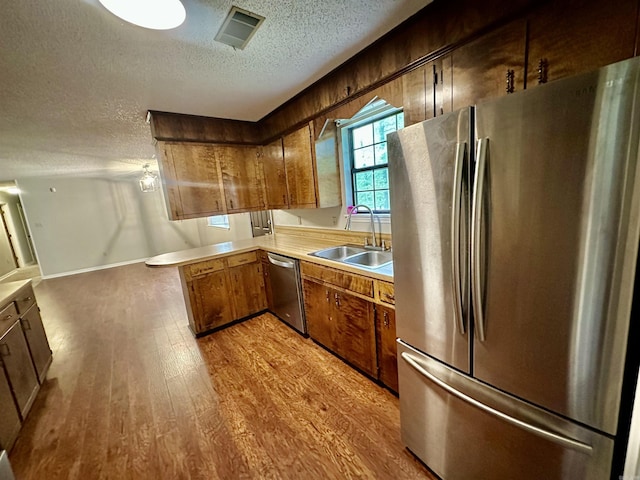 12921 Barth Rd, Alexander, AR 72002 - kitchen featuring appliances with stainless steel finishes, a sink, a textured ceiling, wood finished floors, and a peninsula