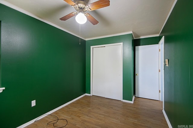 unfurnished bedroom with wood finished floors, a ceiling fan, a closet, baseboards, and ornamental molding