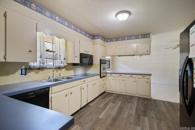 kitchen with dark wood-style flooring, tasteful backsplash, black appliances, and a sink