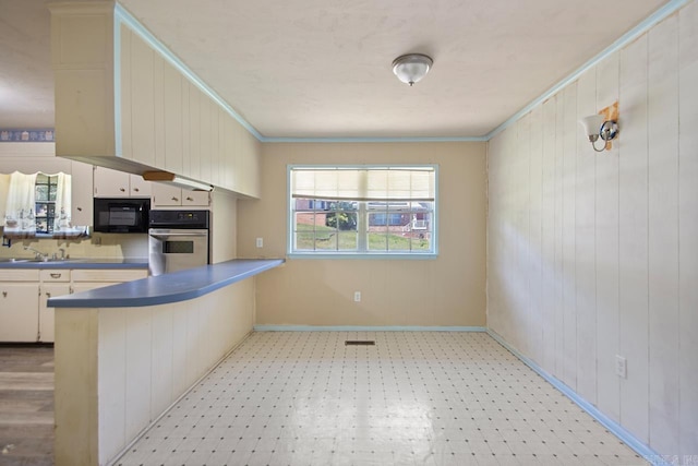 kitchen featuring baseboards, stainless steel oven, black microwave, wooden walls, and a peninsula