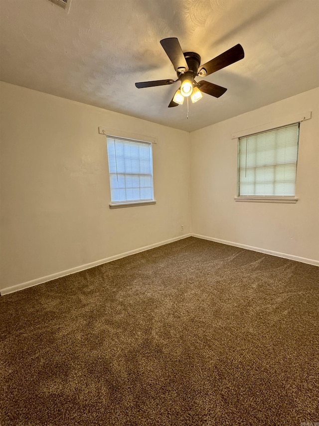 spare room with baseboards, dark carpet, and a ceiling fan
