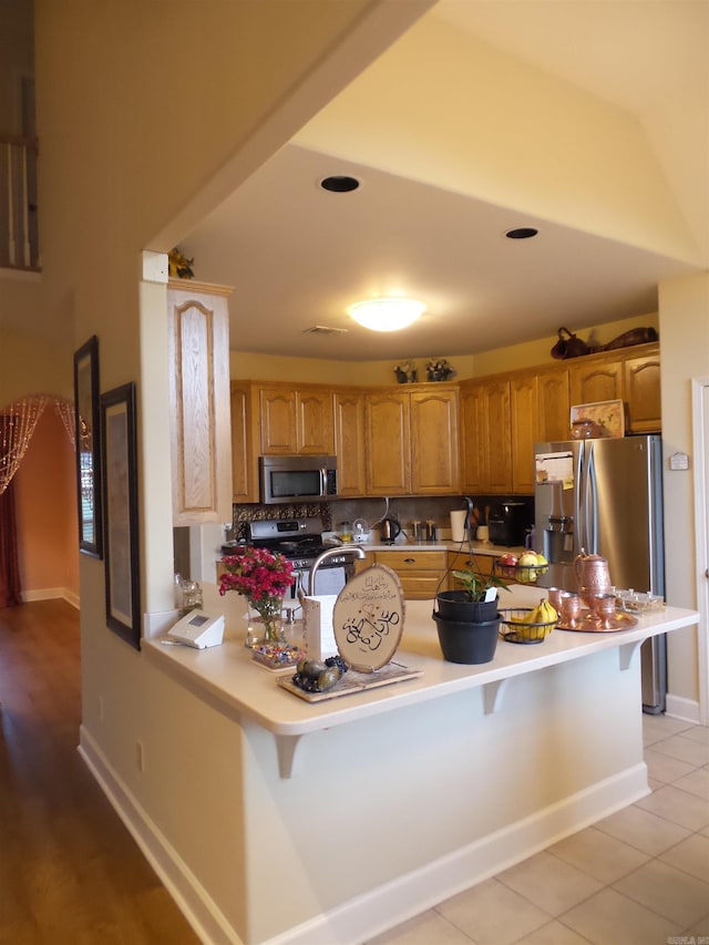2808 Valley Park, Little Rock, AR 72212 - kitchen featuring a peninsula, a breakfast bar area, brown cabinetry, appliances with stainless steel finishes, and tasteful backsplash