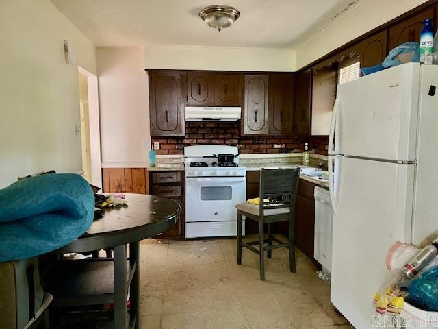 kitchen with white appliances, under cabinet range hood, dark brown cabinetry, decorative backsplash, and light countertops
