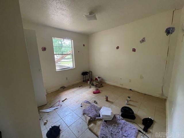 empty room with a textured ceiling, baseboards, and light tile patterned flooring