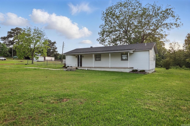 rear view of property with covered porch, a yard, and fence