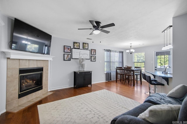 living room with baseboards, a fireplace, wood finished floors, and ceiling fan with notable chandelier