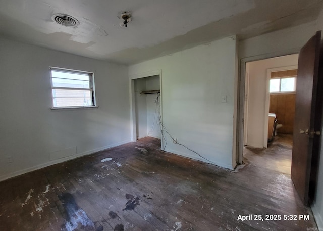 unfurnished bedroom with a closet, visible vents, wood finished floors, and baseboards