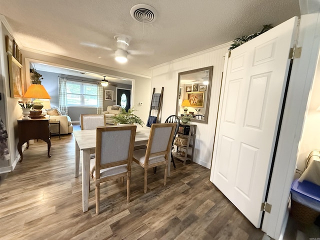 dining room featuring wood finished floors, ornamental molding, a textured ceiling, visible vents, and a ceiling fan