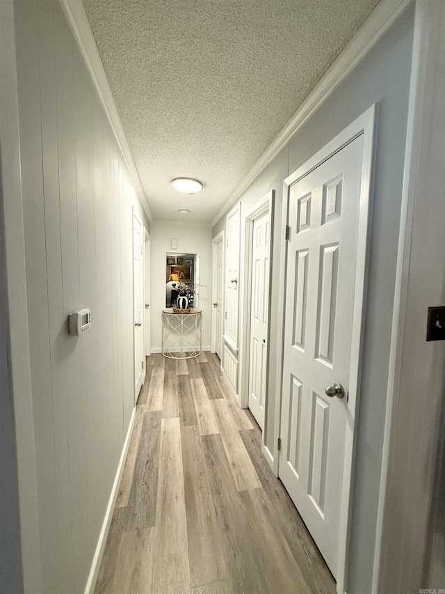corridor with a textured ceiling, wood finished floors, baseboards, and ornamental molding