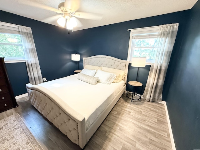 bedroom with a textured ceiling, wood finished floors, baseboards, and multiple windows