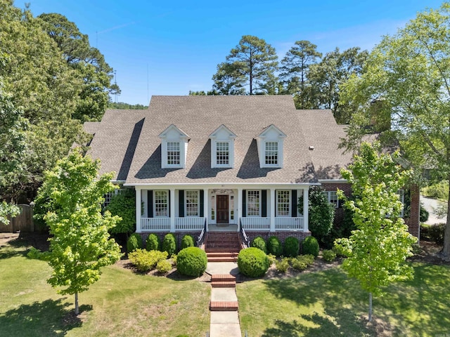 cape cod-style house with covered porch, roof with shingles, fence, and a front yard