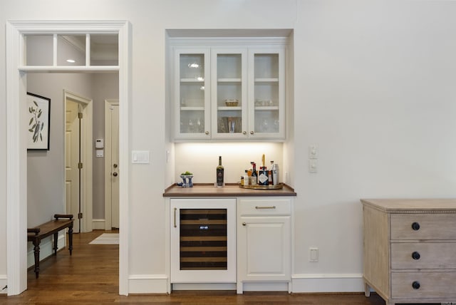 bar featuring dark wood finished floors, beverage cooler, a bar, and baseboards