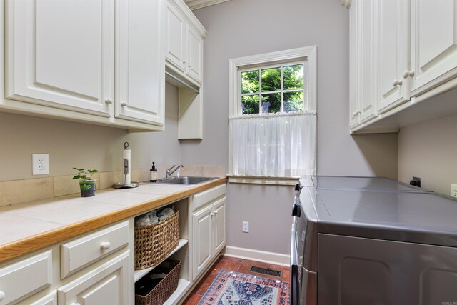 clothes washing area featuring a sink, cabinet space, visible vents, washing machine and clothes dryer, and baseboards