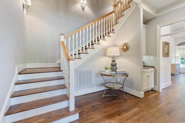 staircase with ornamental molding, baseboards, visible vents, and wood finished floors