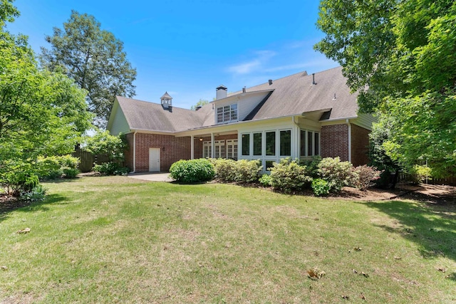 back of property featuring a chimney, brick siding, and a lawn