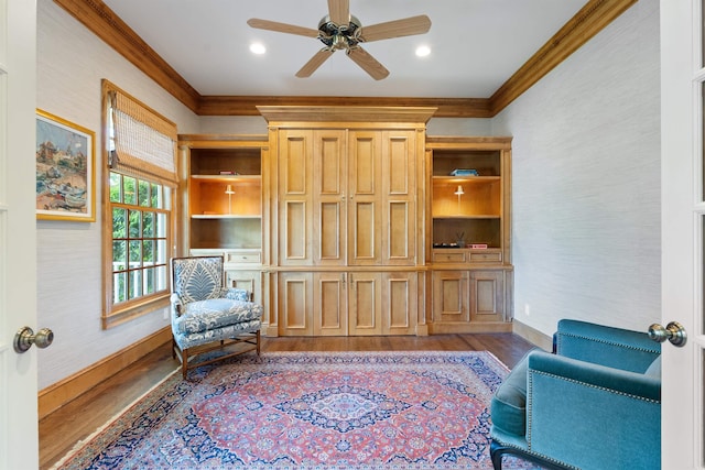 sitting room with baseboards, ceiling fan, crown molding, and wood finished floors