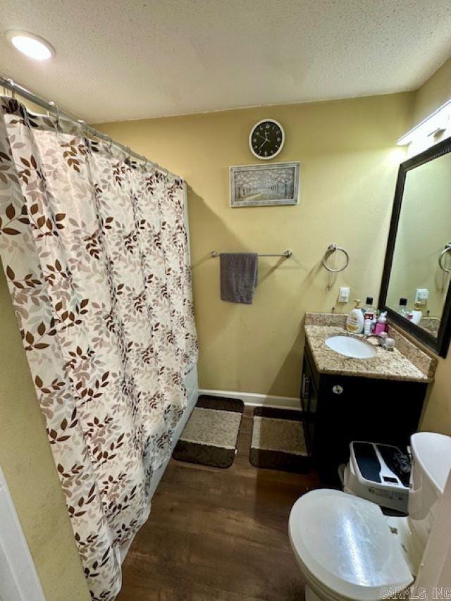 full bathroom featuring toilet, wood finished floors, a textured ceiling, baseboards, and vanity
