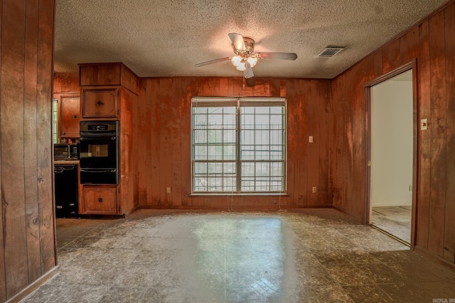unfurnished dining area with ceiling fan, wooden walls, and a textured ceiling