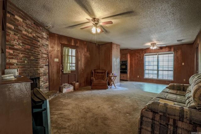 living area with ceiling fan, a textured ceiling, wood walls, and carpet flooring