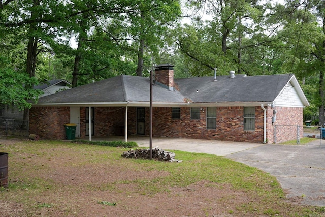 back of house featuring fence, driveway, a chimney, brick siding, and a patio area