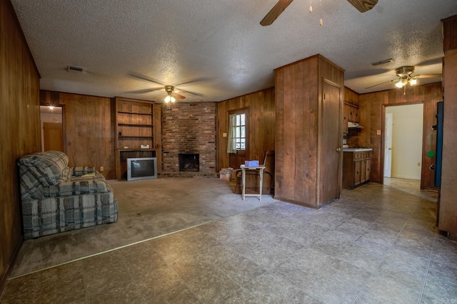 living room featuring ceiling fan, wooden walls, a fireplace, a textured ceiling, and tile patterned floors