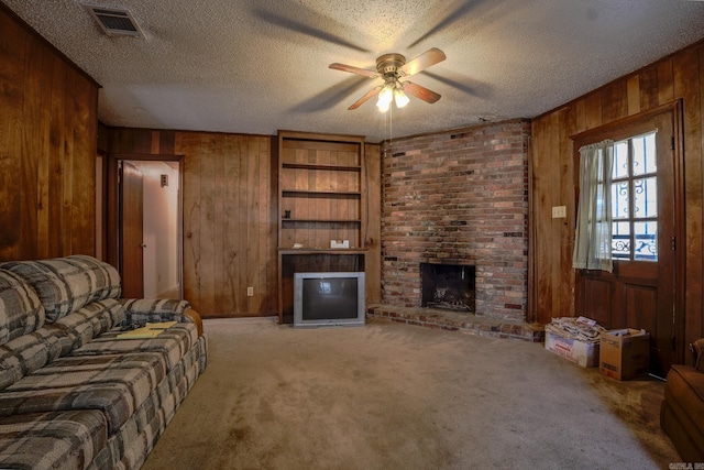 living area featuring wood walls, ceiling fan, a fireplace, a textured ceiling, and carpet flooring