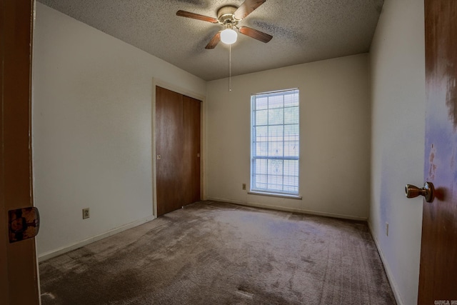 unfurnished bedroom with a textured ceiling, carpet flooring, a closet, a ceiling fan, and baseboards