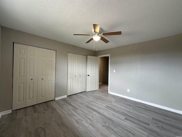 1720 Sanford Dr, Little Rock, AR 72227 - unfurnished bedroom featuring two closets, baseboards, wood finished floors, a textured ceiling, and a ceiling fan