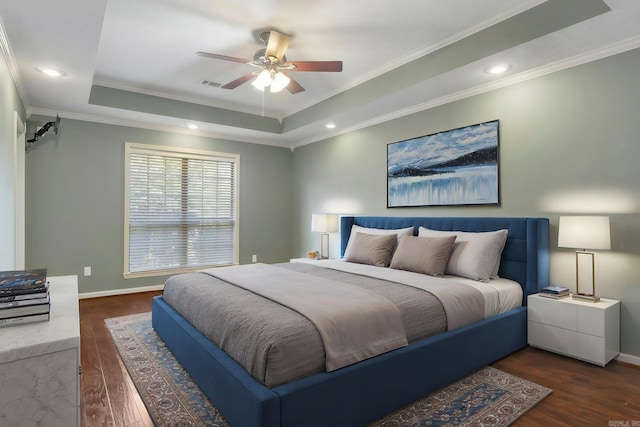 bedroom with a tray ceiling, wood finished floors, ornamental molding, baseboards, and ceiling fan
