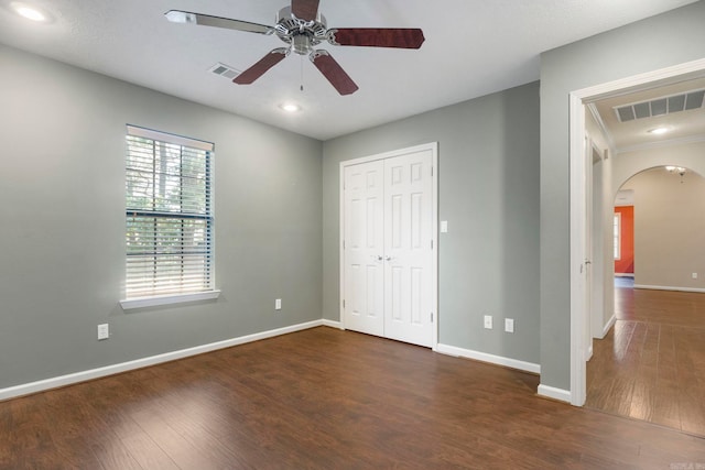 unfurnished bedroom featuring arched walkways, dark wood-style flooring, baseboards, a closet, and ceiling fan