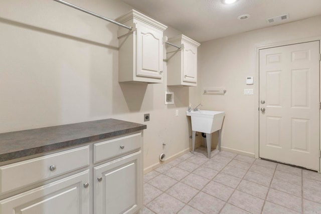 washroom featuring electric dryer hookup, cabinet space, washer hookup, baseboards, and light tile patterned flooring