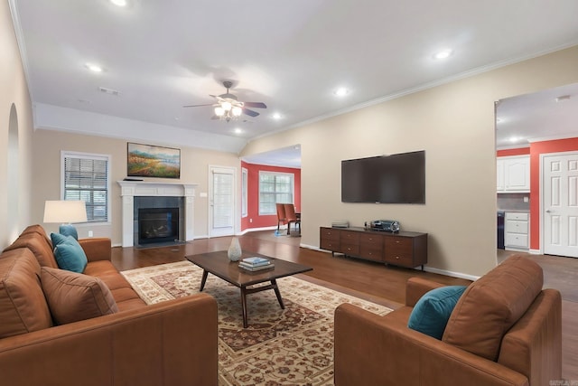 living area with crown molding, ceiling fan, baseboards, wood finished floors, and a tiled fireplace