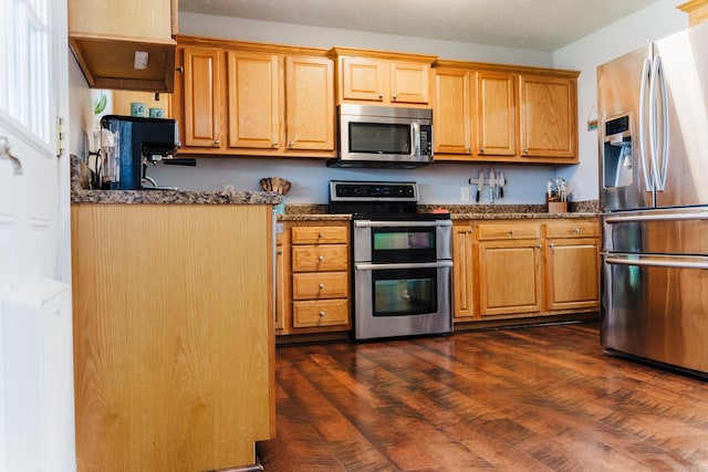 kitchen featuring stainless steel appliances, dark stone counters, and dark wood-type flooring