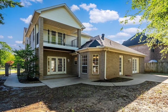 back of house with french doors, a balcony, fence, brick siding, and a patio