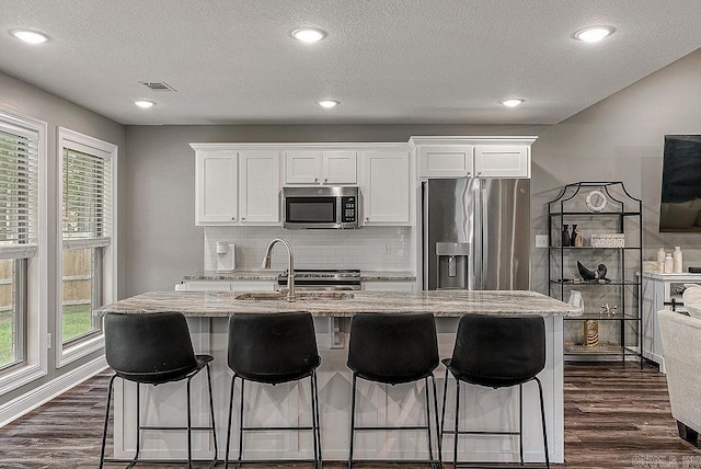 kitchen featuring stainless steel appliances, dark wood-style flooring, decorative backsplash, light stone counters, and white cabinetry