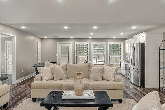living room with dark wood-type flooring, a textured ceiling, baseboards, and recessed lighting