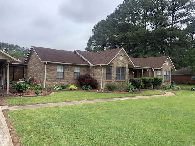 ranch-style house featuring brick siding, a front yard, and roof with shingles