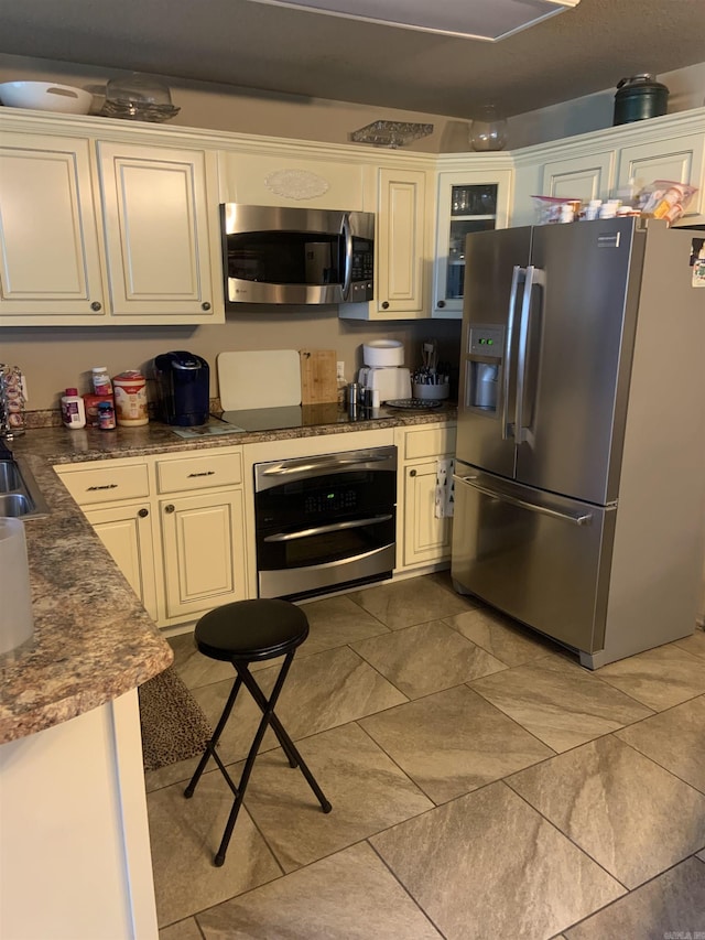 kitchen with stainless steel appliances, dark countertops, a sink, and cream cabinetry